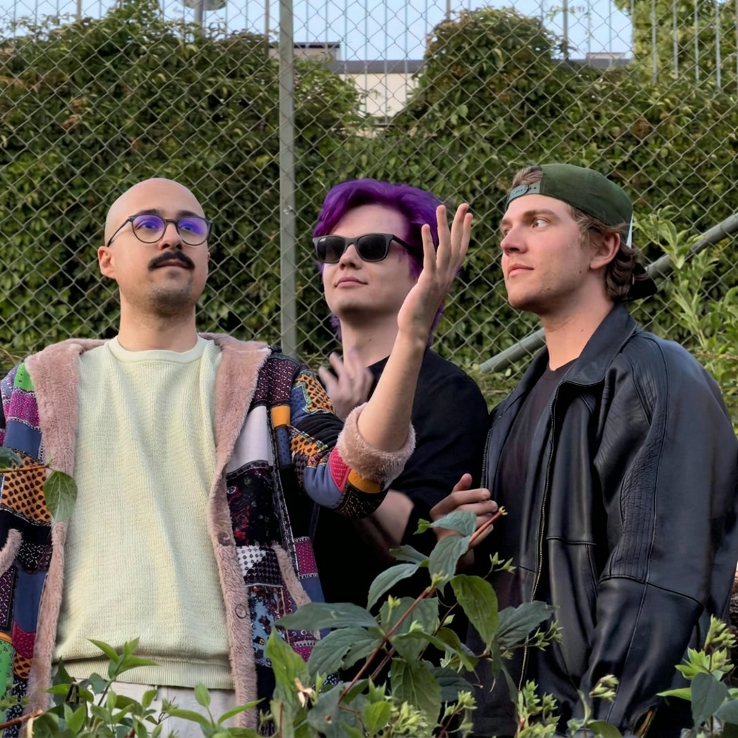 The three members of Kaktus Galaktus posing in front of a chain-link fence